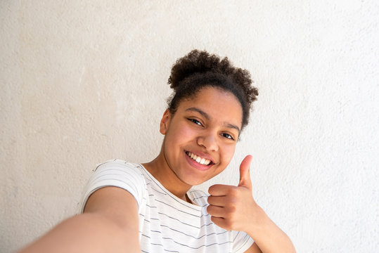 Close Up Happy Young African American Girl Taking Selfie Against White Background With Thumbs Up Hand Sign