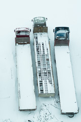 Truck under the snow. lorry covered with snow after snowfall. long trucks stand in a row aerial view. transportation concept. snow covered vehicles. copy space