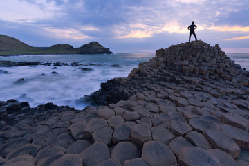 Silhouette of one person standing at Giant Causeway rocks at sunset in Northern Ireland