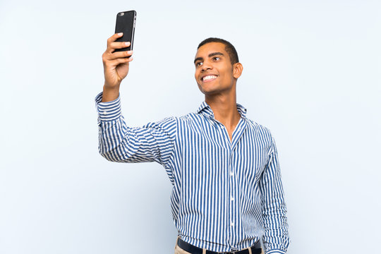 Young handsome brunette man over isolated blue background making a selfie