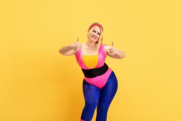 Young caucasian plus size female model's training on yellow background. Copyspace. Concept of sport, healthy lifestyle, body positive, fashion, style. Stylish woman smiling with thumbs up.