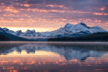 Canadian rockies with foggy reflection on Maligne lake and colorful sky in morning at Jasper...