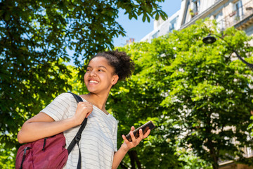 happy young african american school girl with bag and mobile phone walking outside