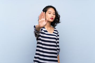 Asian young woman over isolated blue background making stop gesture