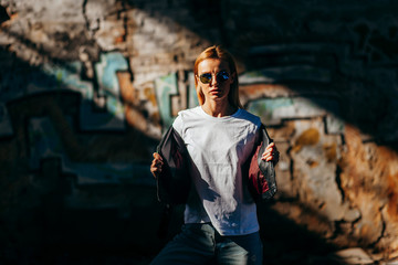 Girl wearing t-shirt, glasses and leather jacket posing against street , urban clothing style....