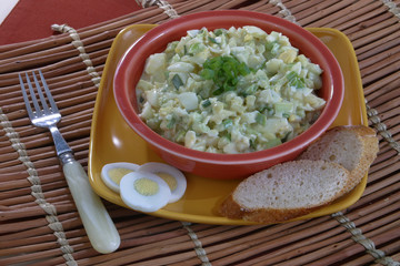 Egg salad in a bowl on at plate with sliced egg and bread