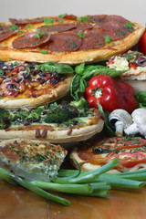 Stack of pizza on a table with peppers, mushroom and scallions