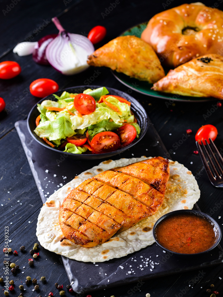 Poster grilled chicken fillet with fresh salad on a dark background