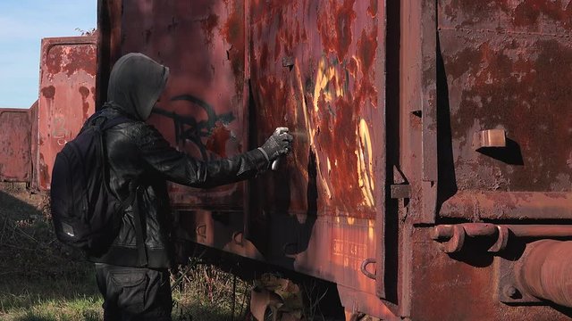 Homeless man spray painting old train wagon with aerosol can