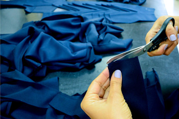 The seamstress cuts the blue fabric with the help of tailor scissors. Cutting material in a sewing workshop. Preparation for sewing clothes. Small business.