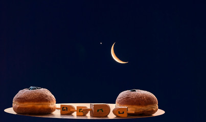 Festive donuts and wooden dreidels are traditional symbols of Hanukkah Holiday. Hebrew letters on four sides of dreidel in English mean - Great Miracle Happened Here