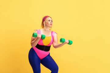 Young caucasian plus size female model's training on yellow background. Copyspace. Concept of sport, healthy lifestyle, body positive, fashion, style. Stylish woman practicing with green weights.