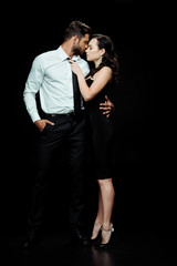 side view of beautiful woman with closed eyes touching tie of man in suit on black