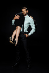 bearded man in suit holding in arms woman in dress isolated on black