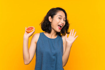 Young asian girl holding a grapefruit over isolated orange background with surprise facial expression