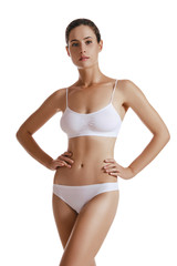 Fototapeta premium Young woman in white underwear, with bundled hair, hands on hips, posing isolated on white. Plastic surgery, aesthetic cosmetology. Close-up shot.