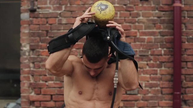 Close view of strong shirtless firefighter putting on yellow oxygen tank
