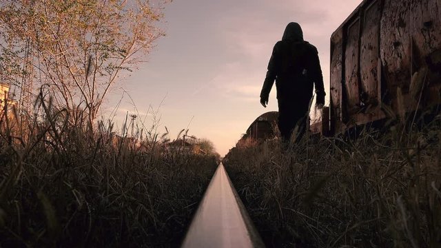 Homeless migrant walking by the rails and abandoned train wagons