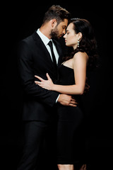 side view of handsome bearded man with closed eyes standing with attractive girl isolated on black