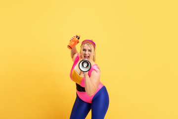 Young caucasian plus size female model's training on yellow background. Copyspace. Concept of sport, healthy lifestyle, body positive, fashion, style. Stylish woman with bottle and mouthpeace.