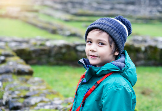 Portrait Of School Kid Explore And Learning About History With School Trip, Happy Child Boy Wearing Hat And Winter Cloths Standing Alone With Blurry Ruins Of Old Abbey Background