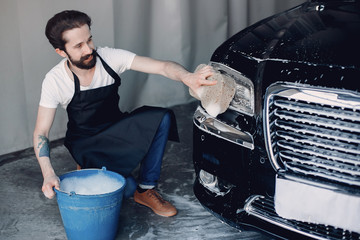 Man in a garage. Worker washing a car. Guy with a bucket ans sponge