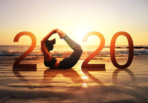 Happy new year card 2020. Silhouette of healthy girl doing Yoga Bow pose on tropical beach with sunset sky background, woman practicing yoga as a part of the Number 2020 sign.