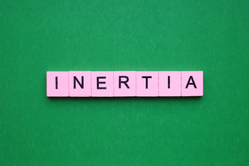 Inertia word wooden cubes on the green background.