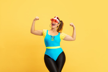 Young caucasian plus size female model's training on yellow background. Copyspace. Concept of sport, healthy lifestyle, body positive, fashion, style. Stylish woman posing confident, girl power.