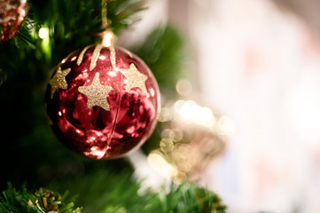 Close up of decoration red  bauble decorated on green Christmas tree or pine with defocused blurred lights bokeh background and copy space. Picture for Xmas eve and happy new year concepts.