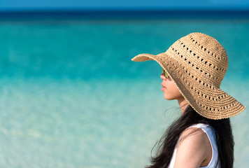 Portrait of young Asian teenager girl with long black hair wearing sunglasses, sun straw hat enjoy vacation with clear blue sea or ocean background. Outdoor summer travelling concept, copy space.