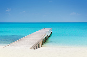 Fototapeta na wymiar Wooden bridge or pier on tropical white sand beach with clear blue sea and sky on sunny day. Boardwalk into the ocean and turquoise water. Summer holidays background with copy space. Kuramathi Island.