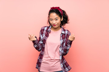 Asian young woman over isolated pink background making money gesture