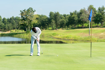 Obraz premium Professional Golfer asian man playing aiming shot for putting ball on the hole with club on green course. Hobby in holiday and vacations in sunny morning day on club golf. Lifestyle and Sport Concept