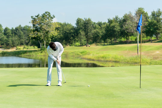 Professional Golfer asian man playing aiming shot for putting ball on the hole with club on green course.  Hobby in holiday and vacations in sunny morning day on club golf. Lifestyle and Sport Concept