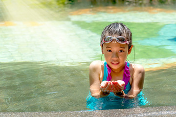 Pretty Asian kid enjoy vacation in swimming pool under sun light. Portrait of preteen girl in...