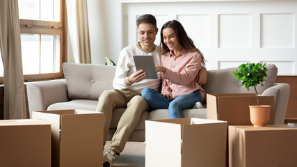 Happy couple using digital tablet sit on sofa with boxes