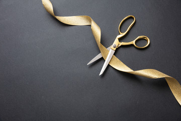 Grand opening. Gold scissors cutting gold satin ribbon, black background - obrazy, fototapety, plakaty