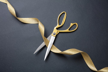 Grand opening. Gold scissors cutting gold satin ribbon, black background