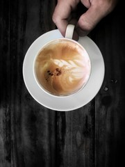 Flat layout of hot coffee cup with coffee art in hand on black wooden background. Selective focus and free space for text.
