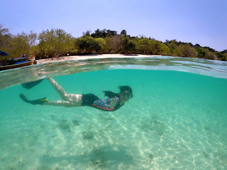 Asian teenager girl enjoy summer vacation on sunny day in crystal clear water. Half underwater of young  healthy woman in colorful swimsuit, mask and black fins relaxing, free diving on turquoise sea.