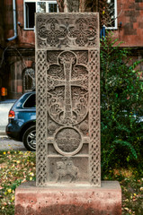 Fototapeta na wymiar Grey stone khachkar with a figured arch over the cross, a figure of a Saint on a horse and a circle-a symbol of eternity on the Alley of stone crosses in Gyumri