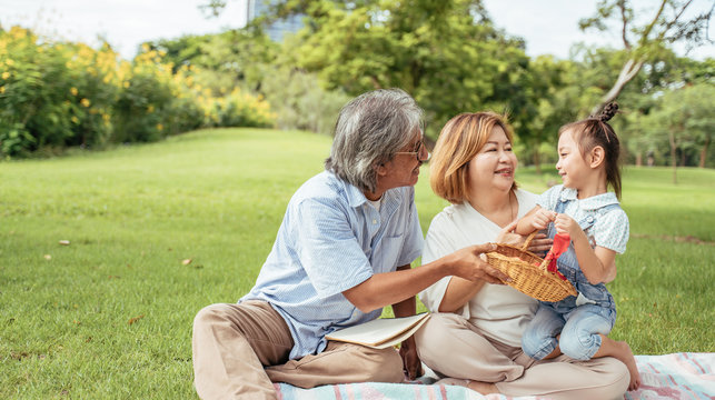 Grandmother,Grandfather And Grand Daughter Enjoying Sunny Garden Holiday Together, Outdoors Space, Leisure Lifestyle,happy Teaching With Flare Light Sky In Park.