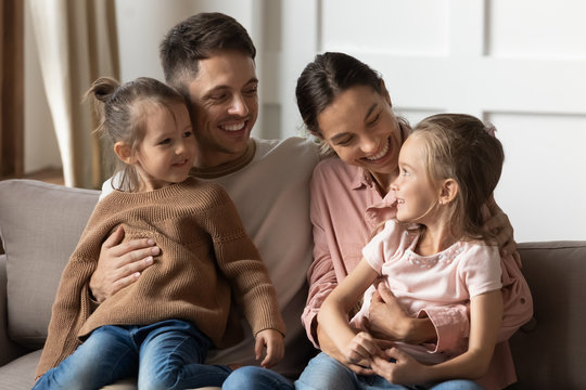 Happy loving parents holding children on lap relax on couch
