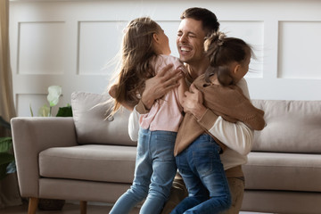 Cheerful dad embracing kids daughters cuddling at home celebrate reunion