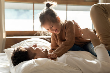 Cute kid daughter playing with dad on bed in morning