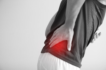 Young man suffering from back pain on light background, closeup