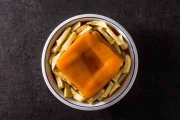 Typical Portuguese francesinha sandwich with french fries on black background. Top view