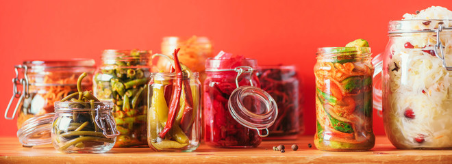 Assortment of various fermented and marinated food over wooden background, copy space. Fermented vegetables, sauerkraut, pepper, garlic, beetroot, korean carrot, cucumber kimchi in glass jars.