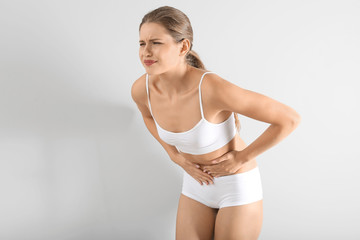 Young woman suffering from abdominal pain on grey background. Gynecology concept